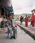 man sitting in front of his small shop,  while woman are taking care of the Yaks at the mountain top, Tagong Sichuan